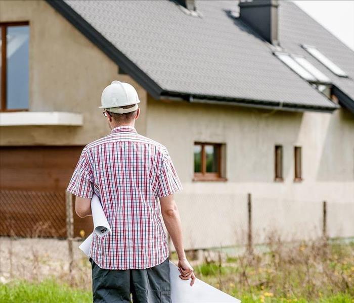 A contractor holding a paper while walking towards a house.